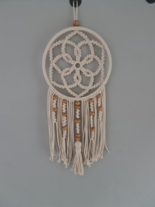 Adorno de parede em macramê com design único em formato de mandala, combinando sofisticação e aconchego. Feito artesanalmente com técnicas tradicionais e materiais resistentes, inclui detalhes em contas de madeira que realçam seu charme rústico. Versátil,