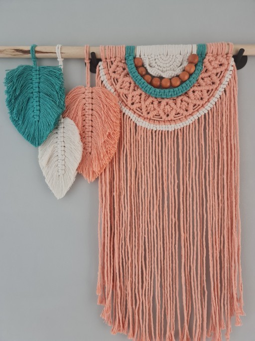 Adicione um toque de elegância boho e calor artesanal ao seu espaço com este deslumbrante pendente de parede em macramê. Cuidadosamente feito à mão, esta peça única combina fios de algodão em tons suaves de pêssego, branco e turquesa.